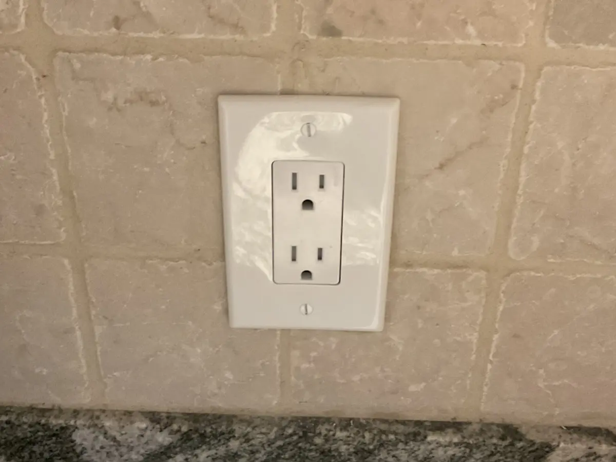 Installed kitchen electrical outlet with white cover plate.