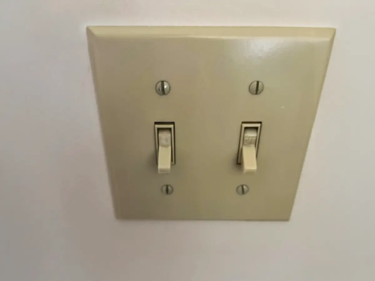 Outdated dual switch plate with toggle light switches in beige.