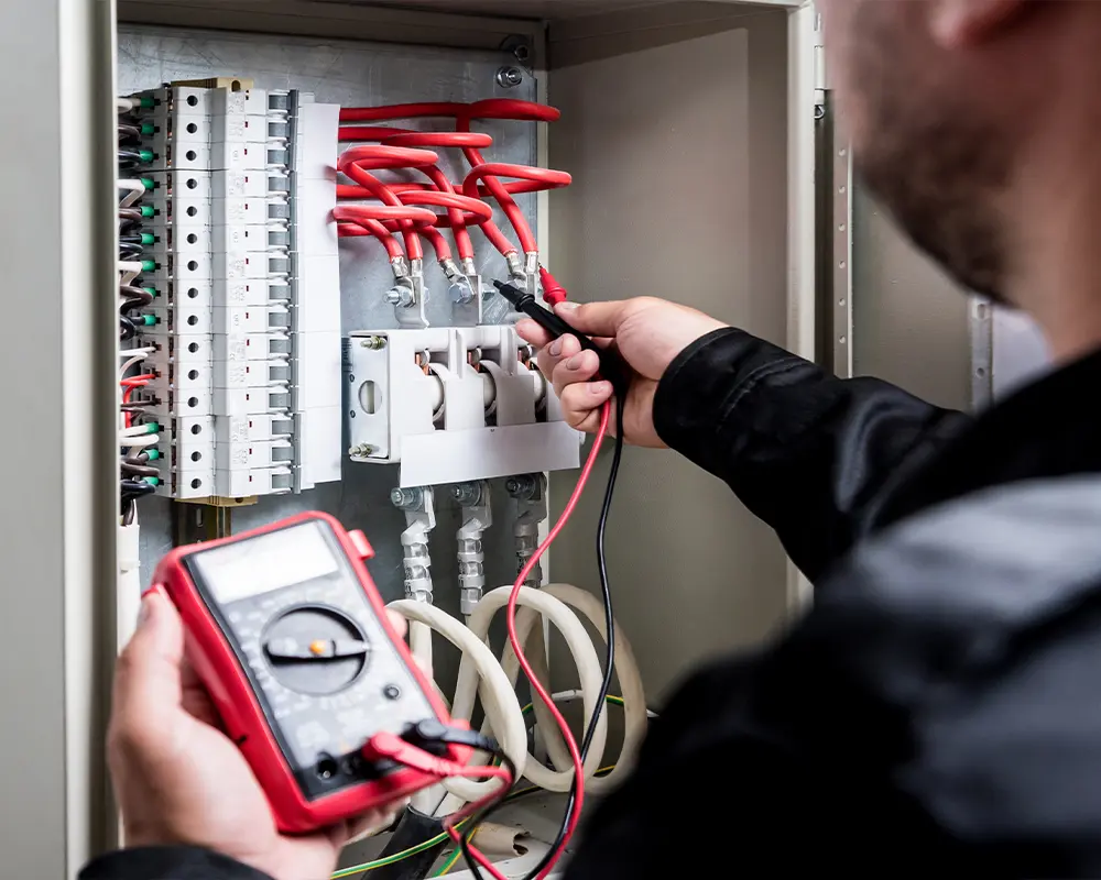 Electrician testing breaker panel wiring for electrical safety.