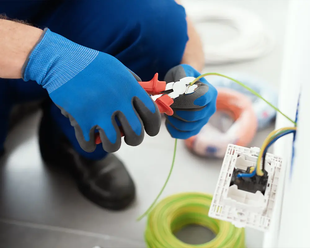 Electrician wearing gloves, cutting electrical wire for safe installation in residential setup.