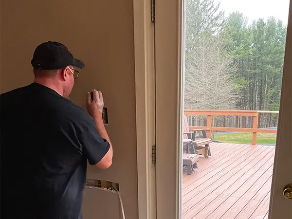 Electrician working on light switch installation near patio door with deck view.