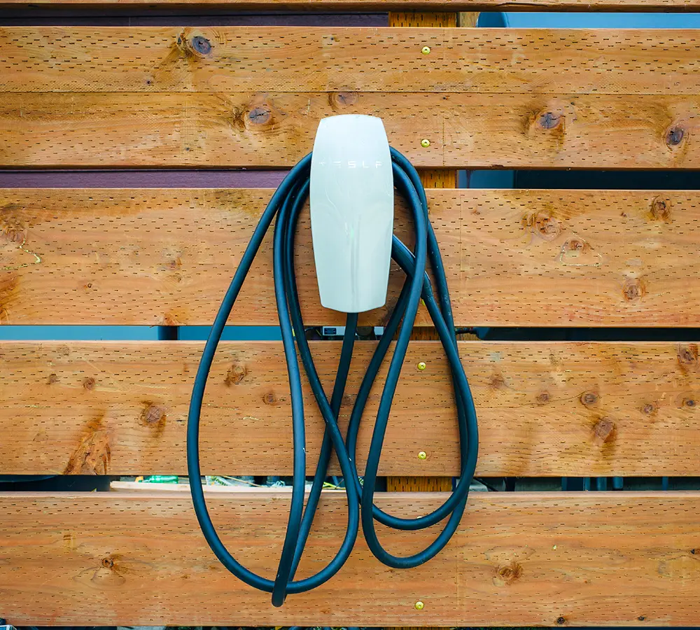 Tesla wall charger with cable coiled on wooden fence, installed for outdoor EV charging.