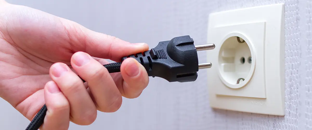 Hand plugging black electrical cord into wall socket for power connection.