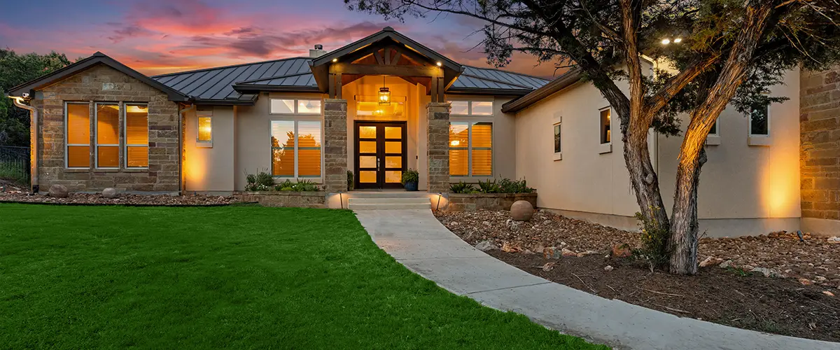 Modern single-story house with exterior lighting at dusk and a well-maintained lawn.